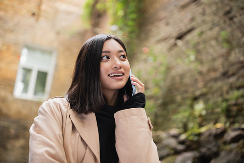 Positive asian woman talking on mobile phone in outdoor cafe