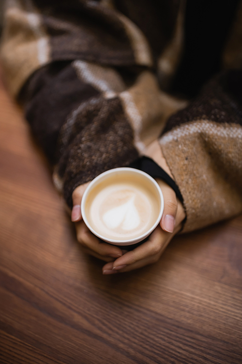 Top view of woman in blanket holding cappuccino in outdoor cafe