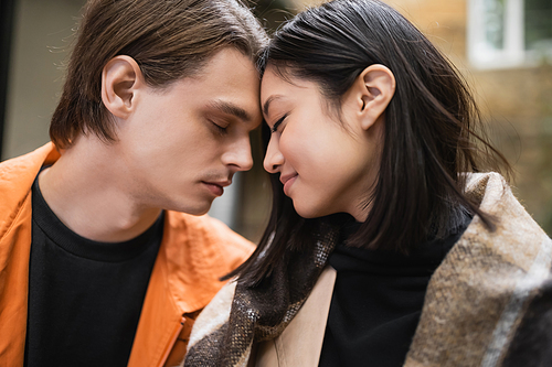 Side view of smiling interracial couple with blanket standing with closed eyes outdoors