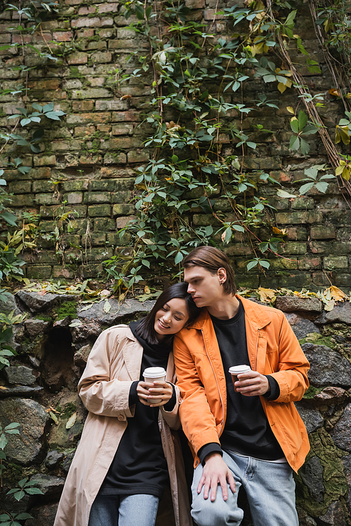 Smiling asian woman holding takeaway drink while standing near boyfriend on urban street