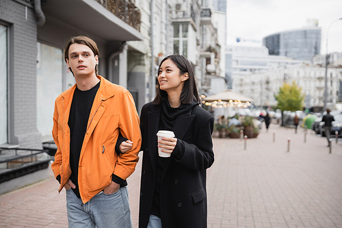 Stylish young interracial couple with coffee to go walking on urban street