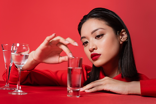 young asian woman with makeup touching glass with pure  isolated on red