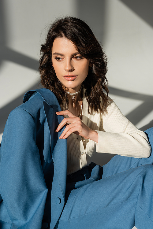 pretty brunette woman with blue jacket looking away while sitting on grey background with lighting and shadows