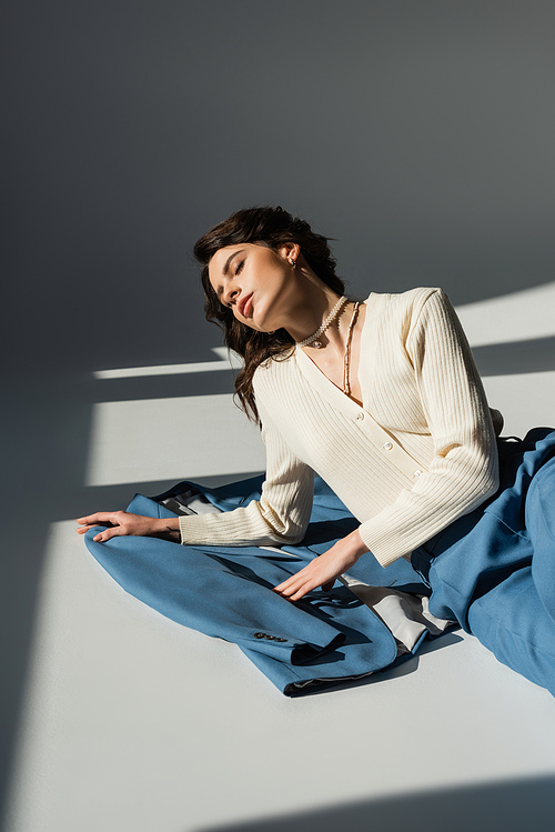 high angle view of brunette woman in jumper lying near blue blazer on grey background with sunlight