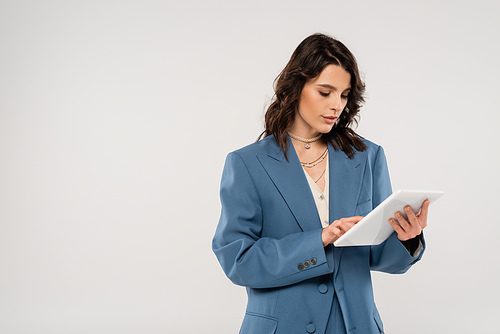 young woman in blue fashionable jacket using digital tablet isolated on grey