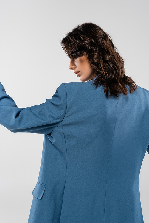 back view of brunette woman in blue blazer posing isolated on grey