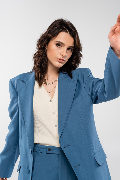 young fashionable woman in blue suit looking at camera while posing isolated on grey