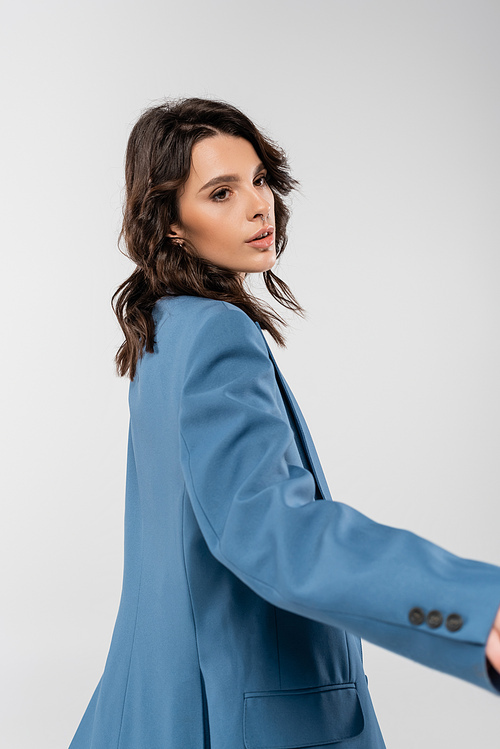 young brunette woman in blue and trendy jacket looking away isolated on grey