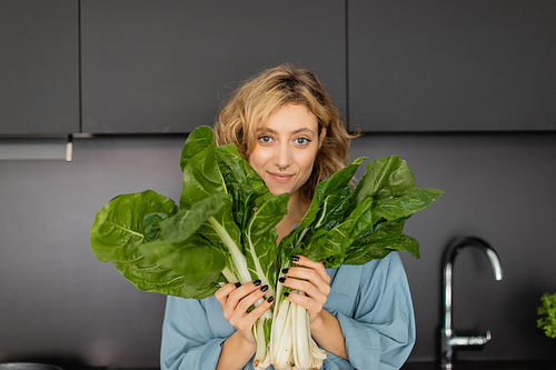 pierced young woman smiling and holding green cabbage leaves in kitchen