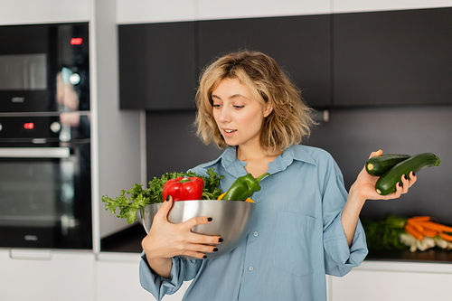 young woman with wavy hair looking at bowl with fresh vegetables in kitchen