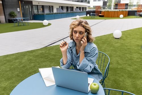 pensive woman talking on smartphone near laptop on bistro table in Barcelona