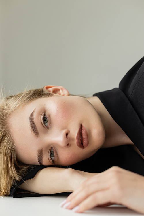 portrait of blonde woman with natural makeup on perfect face lying on white surface isolated on grey