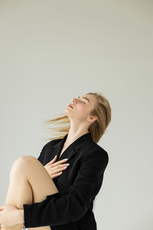 blonde model in black blazer posing with closed eyes isolated on grey