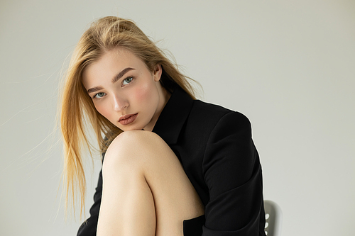 blonde woman in black blazer looking at camera isolated on grey