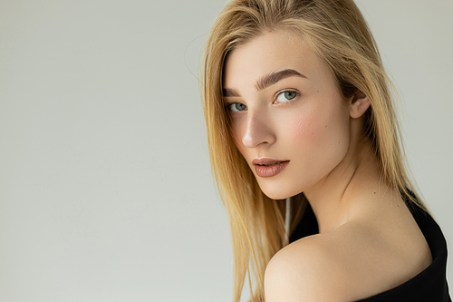 portrait of blonde woman with perfect skin and natural makeup looking at camera isolated on grey