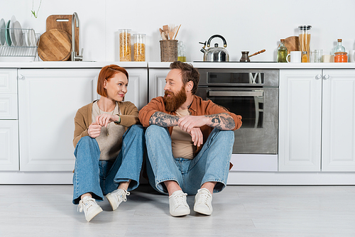 Smiling adult couple looking at each other while sitting on floor in kitchen