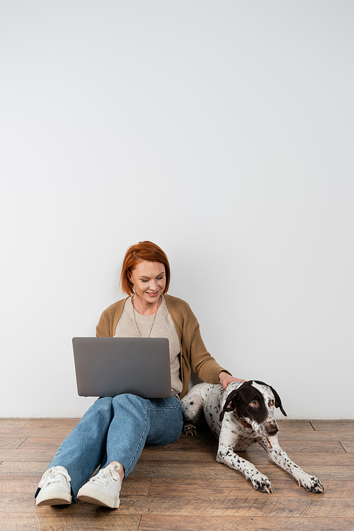 Smiling freelancer with laptop petting dalmatian at home
