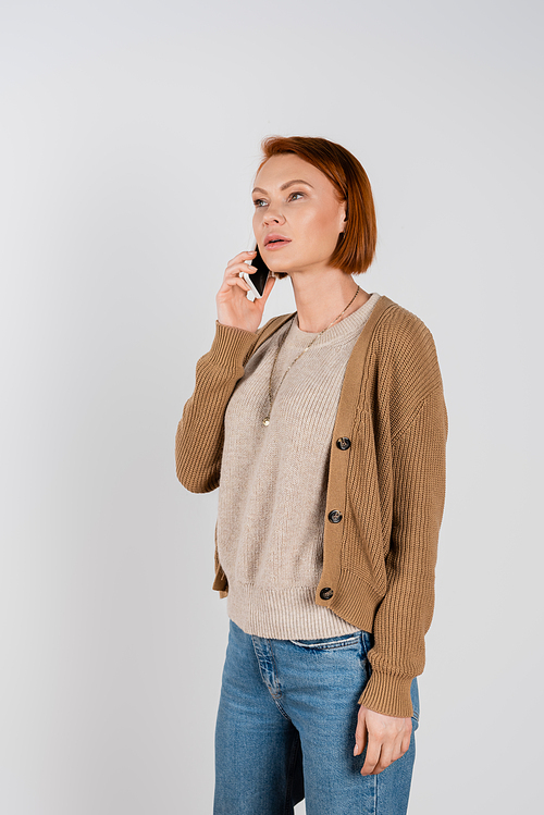 Redhead woman in casual clothes talking on smartphone isolated on grey