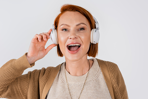 Portrait of red haired woman singing while using headphones isolated on grey