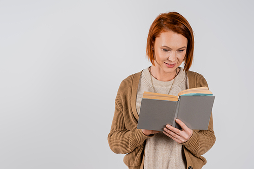 Smiling redhead woman reading book isolated on grey