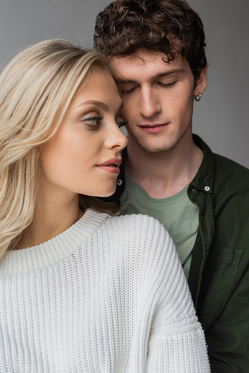 portrait of curly young man with closed eyes near blonde woman in white sweater