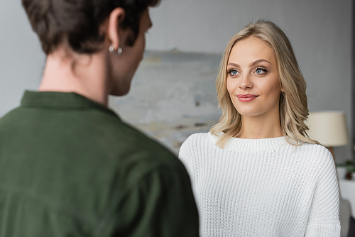 pleased blonde woman with blue eyes looking at curly man in shirt on blurred foreground