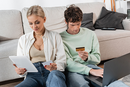 young man and woman holding gadgets and credit cards while doing online shopping