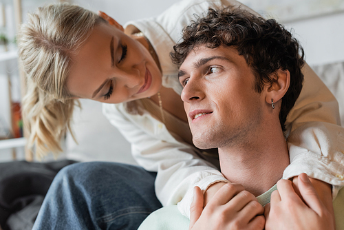 smiling and blonde woman embracing curly man in living room