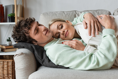 happy young man embracing girlfriend while lying on couch in living room
