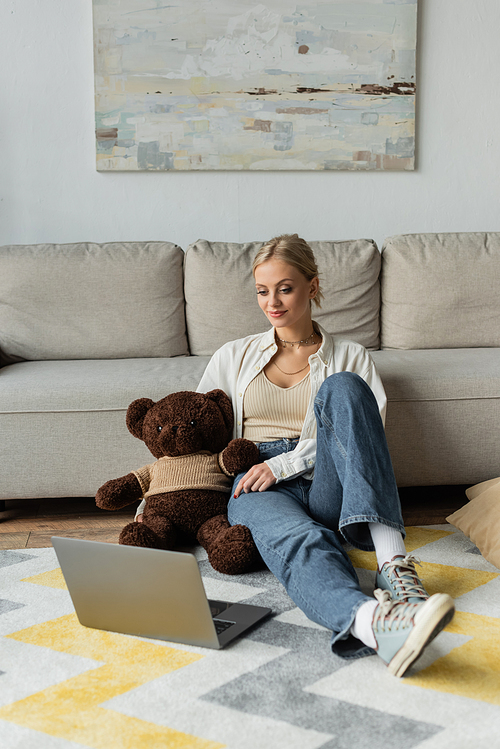 young woman in jeans holding teddy bear and watching movie on laptop