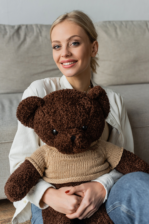 positive young woman holding teddy bear and looking at camera
