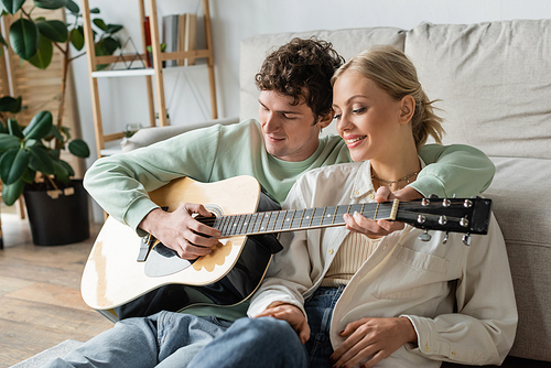 curly man playing acoustic guitar near cheerful blonde woman