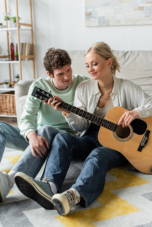 cheerful blonde woman playing acoustic guitar near curly boyfriend