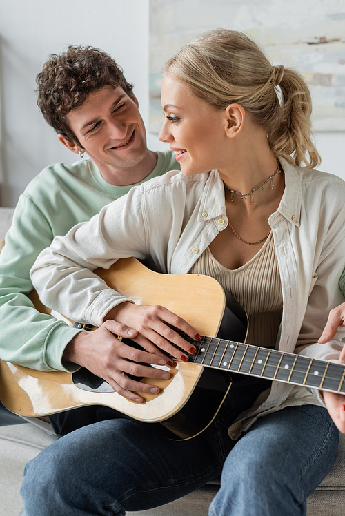 happy young couple playing acoustic guitar while sitting on couch