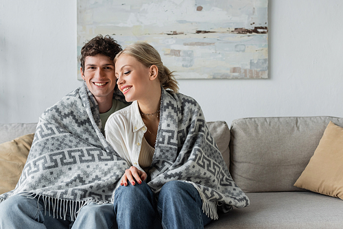 happy young man and woman covered in blanket sitting on couch