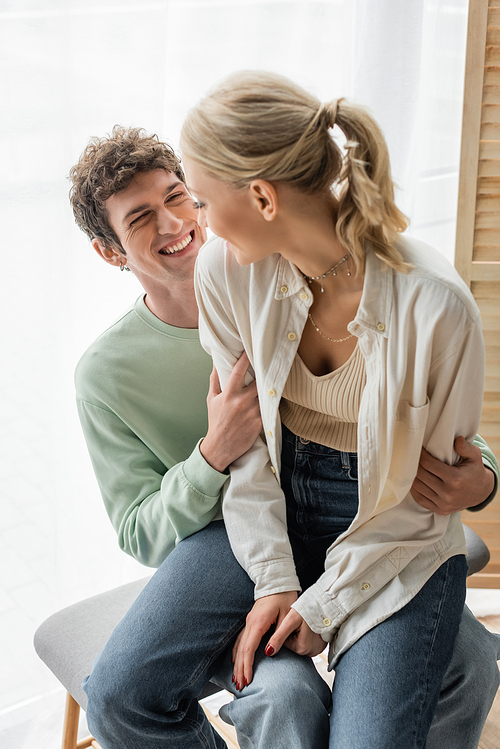 cheerful woman sitting with happy boyfriend on bed bench