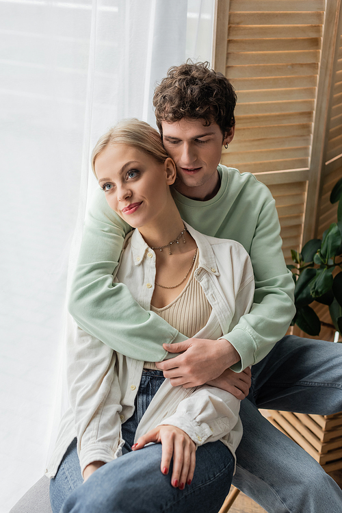 curly man hugging young blonde girlfriend in shirt and jeans