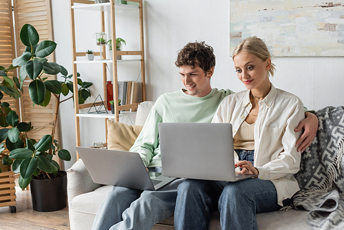 cheerful man and woman using laptops while working from home in living room