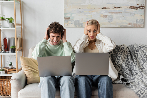 stressed young man and woman looking at laptops while sitting on couch