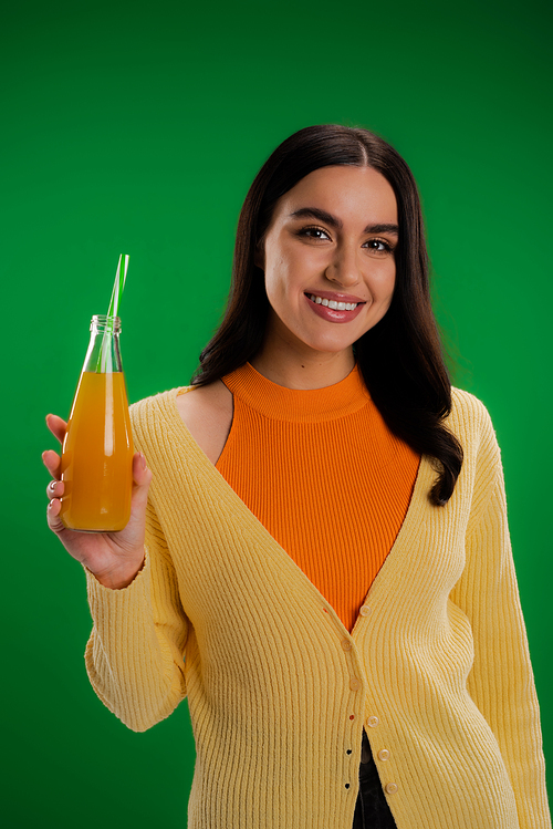 happy brunette woman holding bottle of fresh juice with straw isolated on green