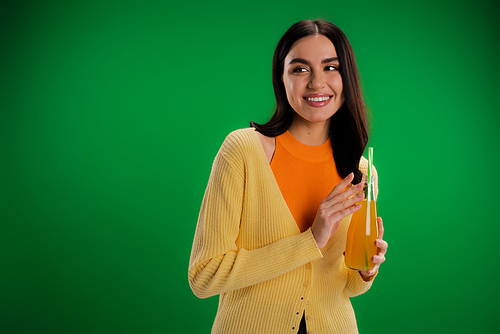 stylish woman with bottle of fresh juice smiling and looking away isolated on green