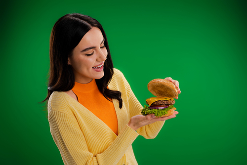 amazed woman looking at tasty burger with cheese and meat isolated on green