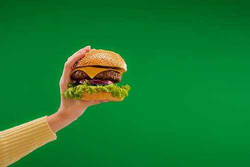 partial view of woman holding tasty burger with lettuce and cheese with meat isolated on green