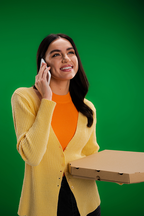 happy young woman calling on smartphone while standing with pizza box isolated on green