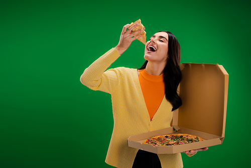 young woman with open mouth holding carton box and delicious pizza isolated on green