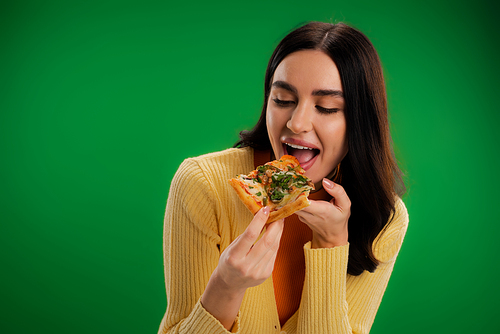pretty brunette woman eating tasty pizza isolated on green