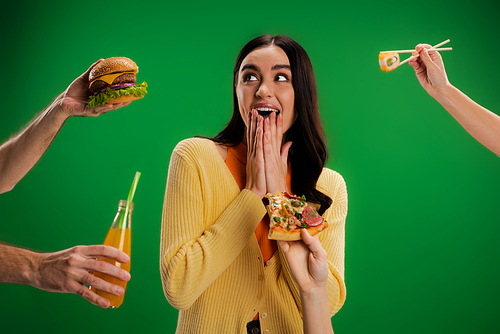 astonished woman covering mouth with hands near people proposing different food isolated on green