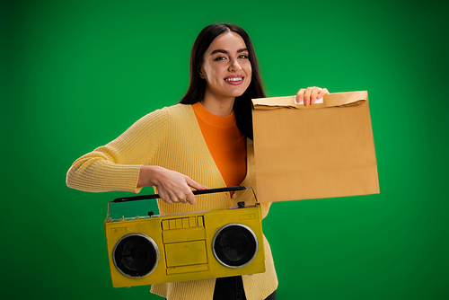 happy woman holding boombox and food package isolated on green