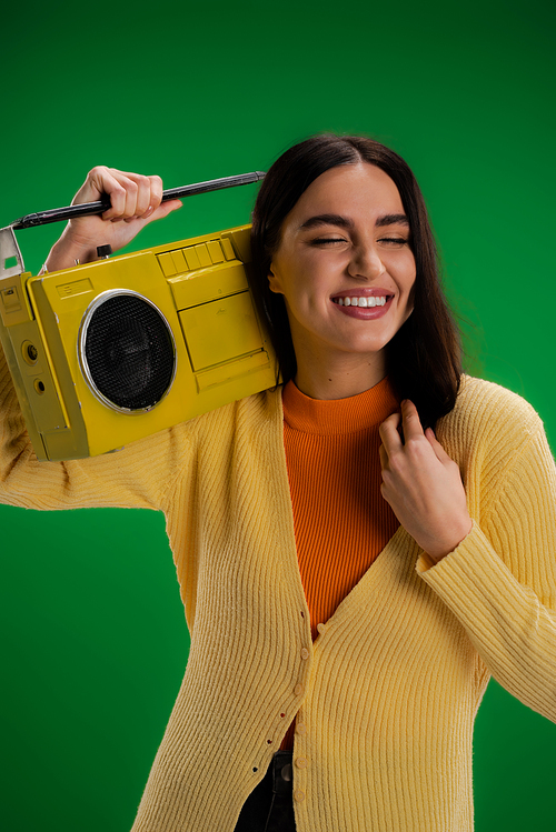 cheerful woman with closed eyes holding vintage boombox isolated on green