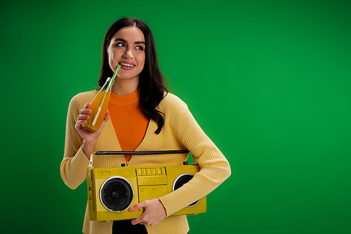 smiling woman with boombox drinking soda and looking away isolated on green